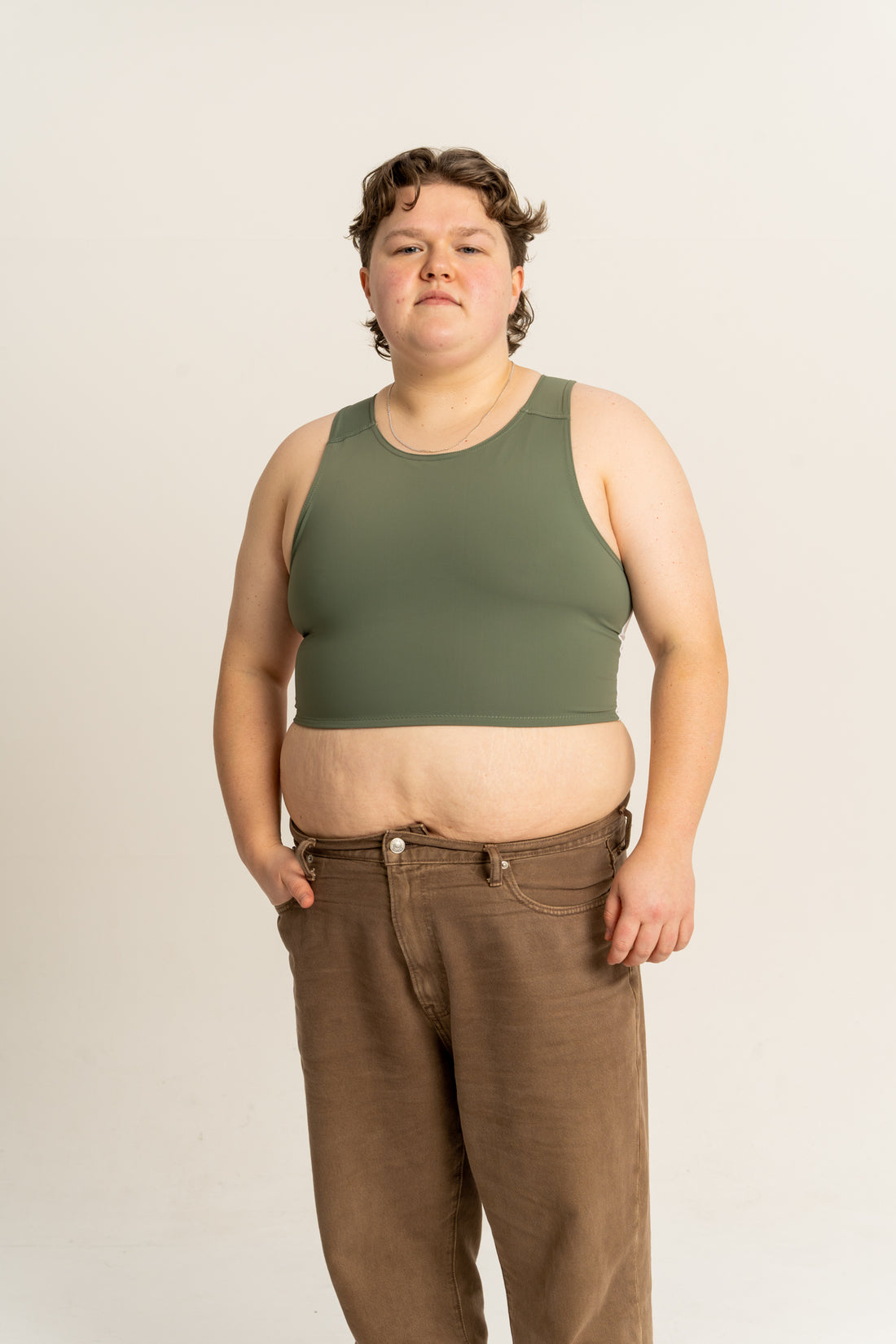 Person wearing a green chest binder light and brown trousers against a white background