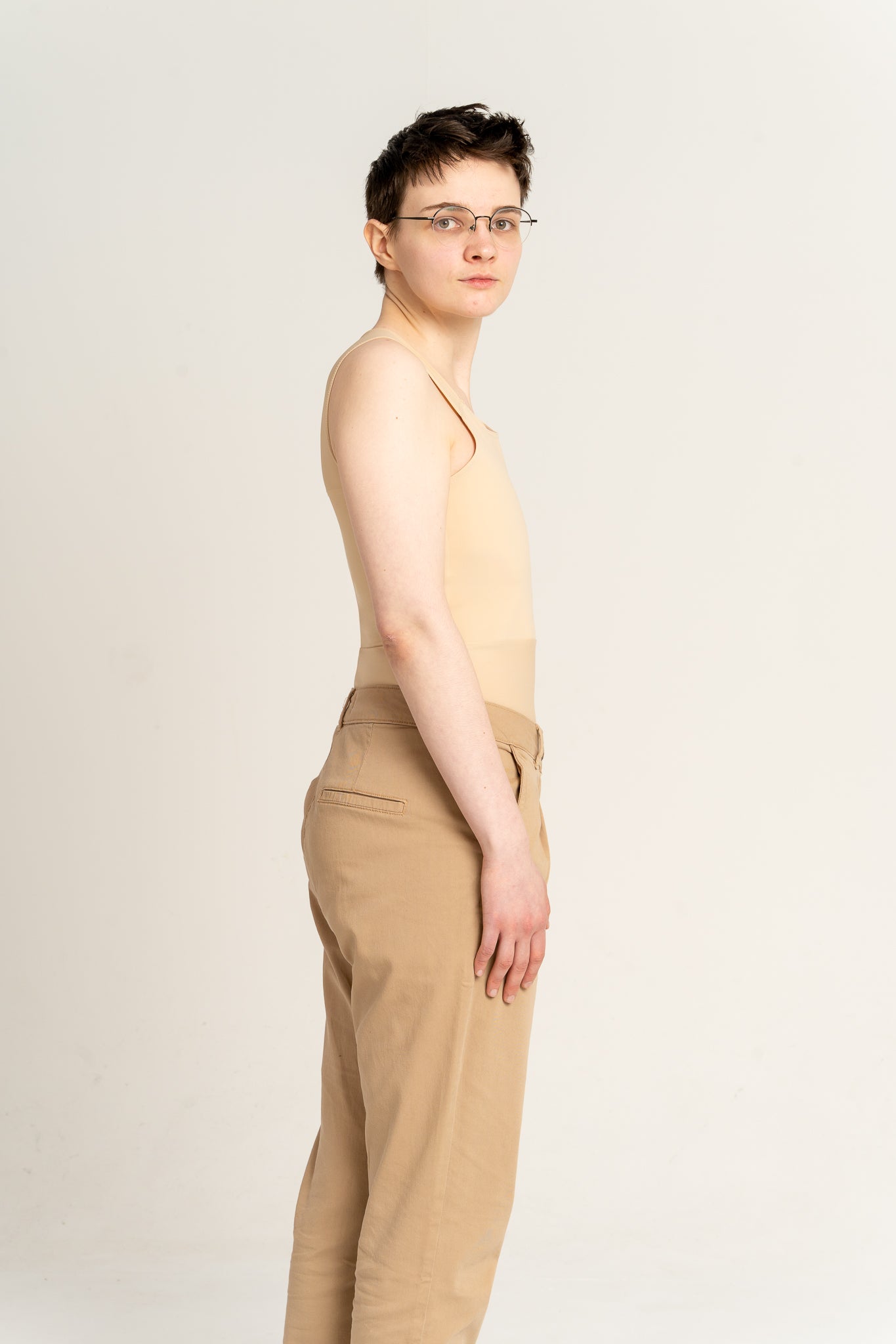 Person wearing a fair long chest binder and tan coloured trousers against a white background