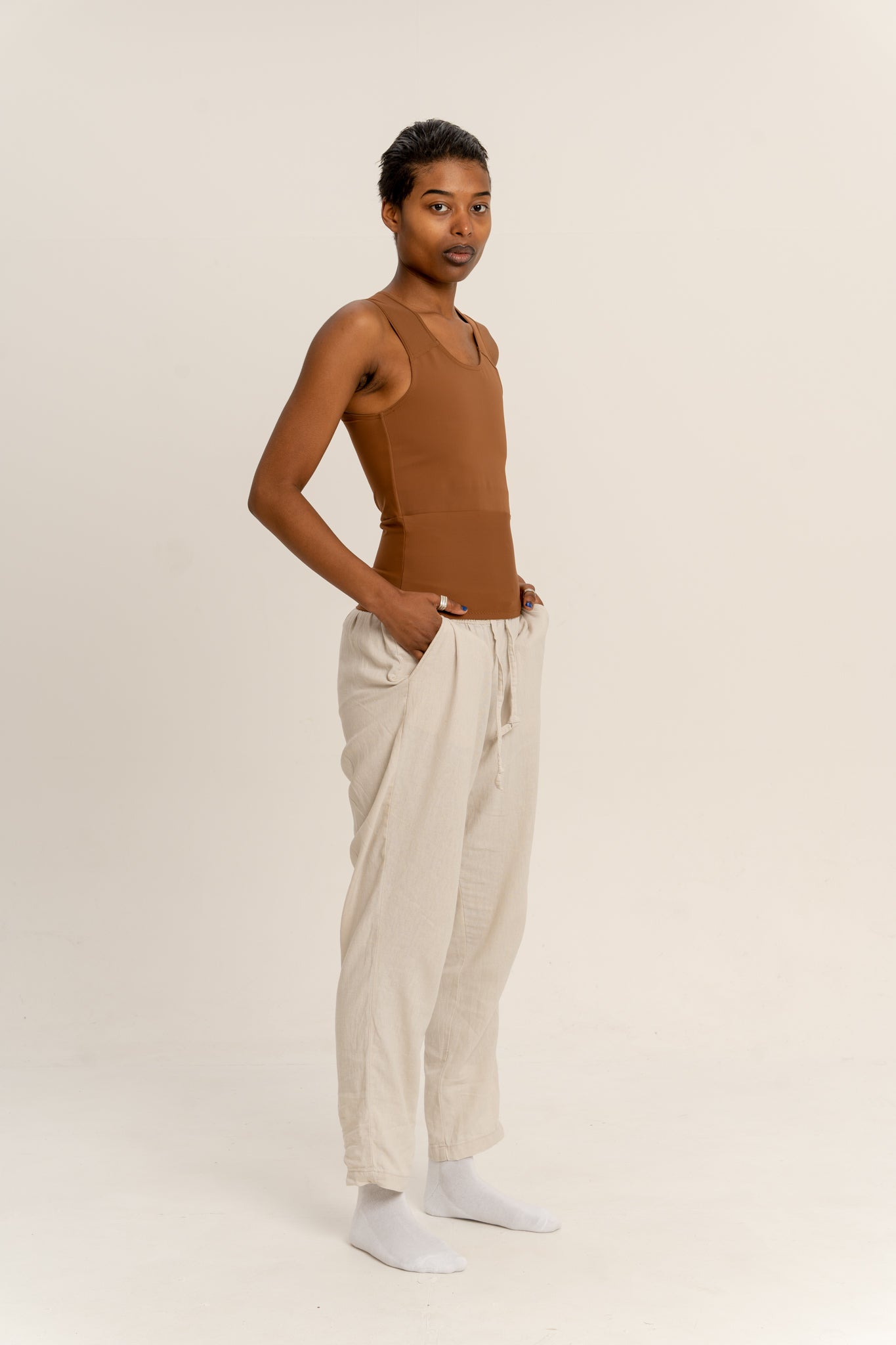 Person wearing a deep long chest binder and beige trousers against a beige background