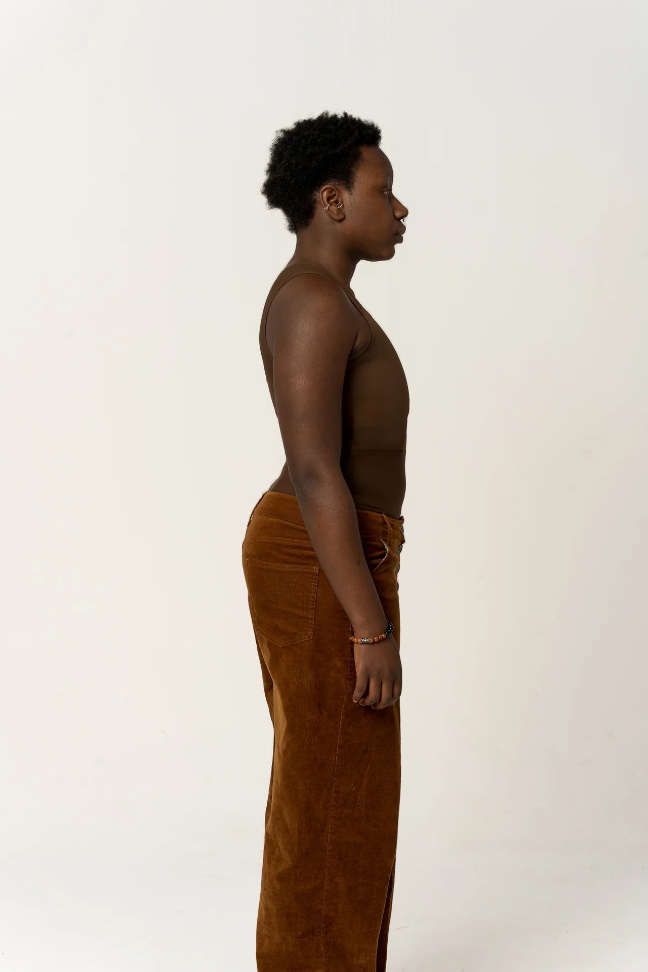 Person wearing a long dark chest binder and brown trousers facing to the side.