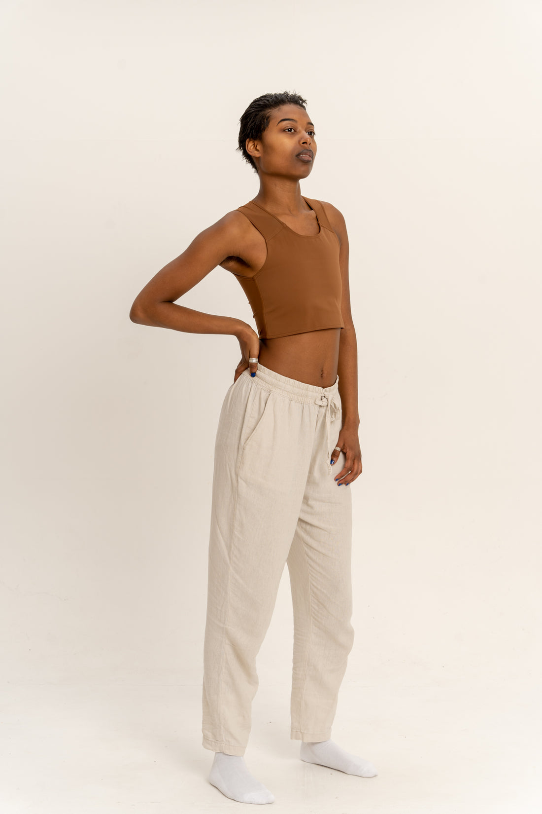 Person wearing a deep short chest binder and beige pants against a white background