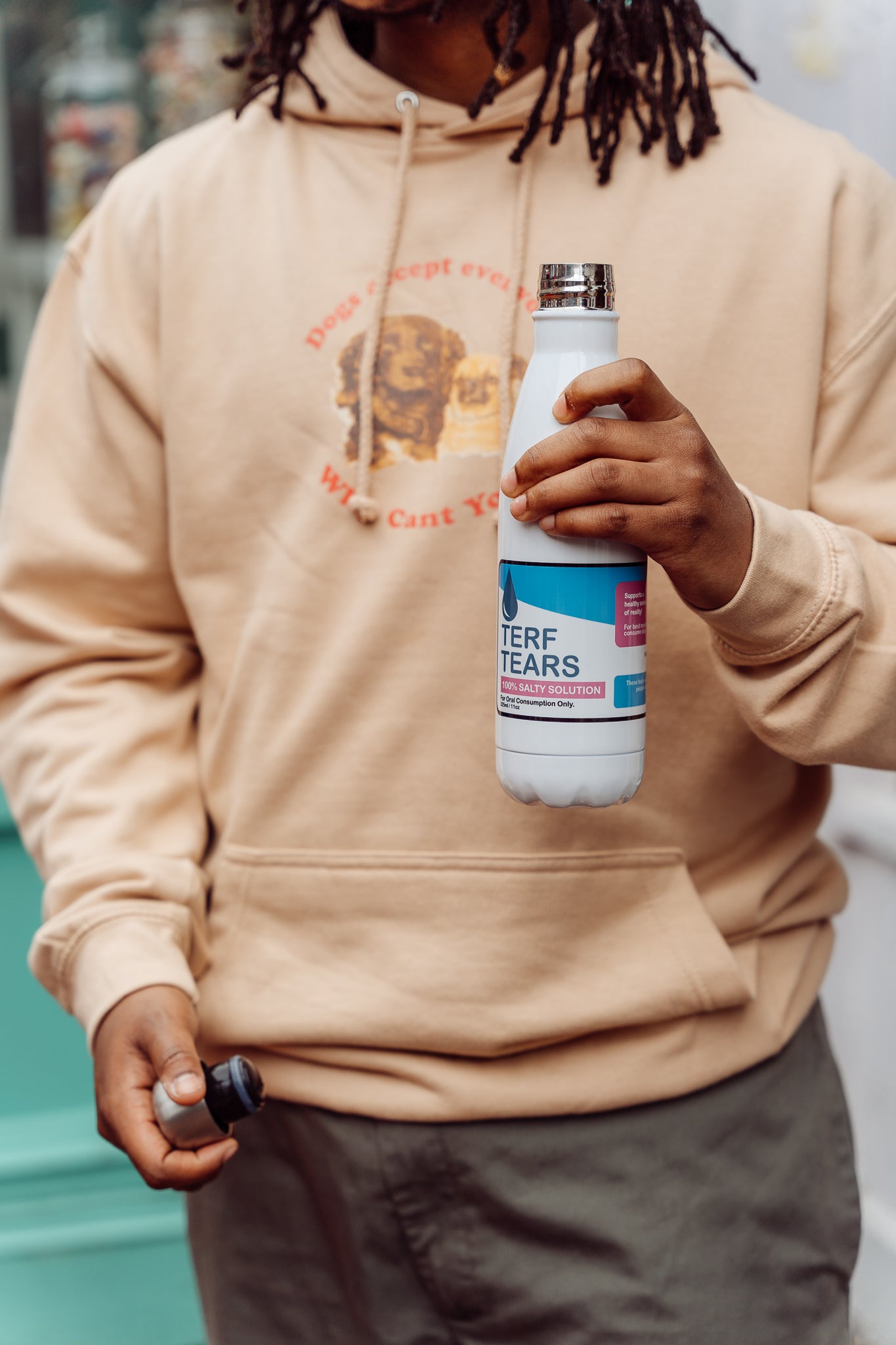 Person wearing a beige hoodie holding a bottle labeled 'Terf Tears'.