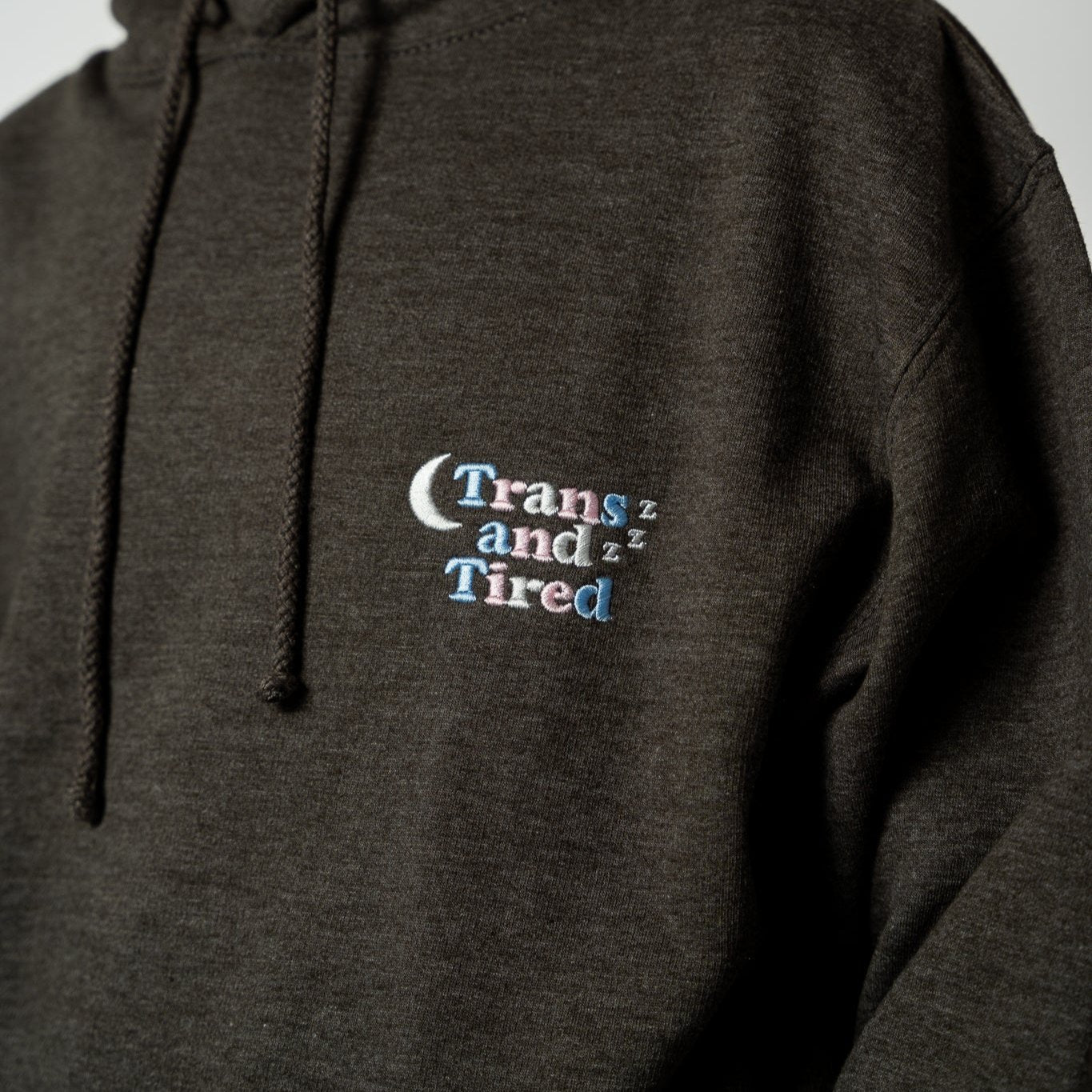 Dark gray hoodie with 'Trans and Tired' text on the chest.