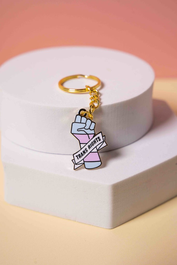 Keychain with a raised fist and a banner with 'Trans Rights' text on a white base with a pink background