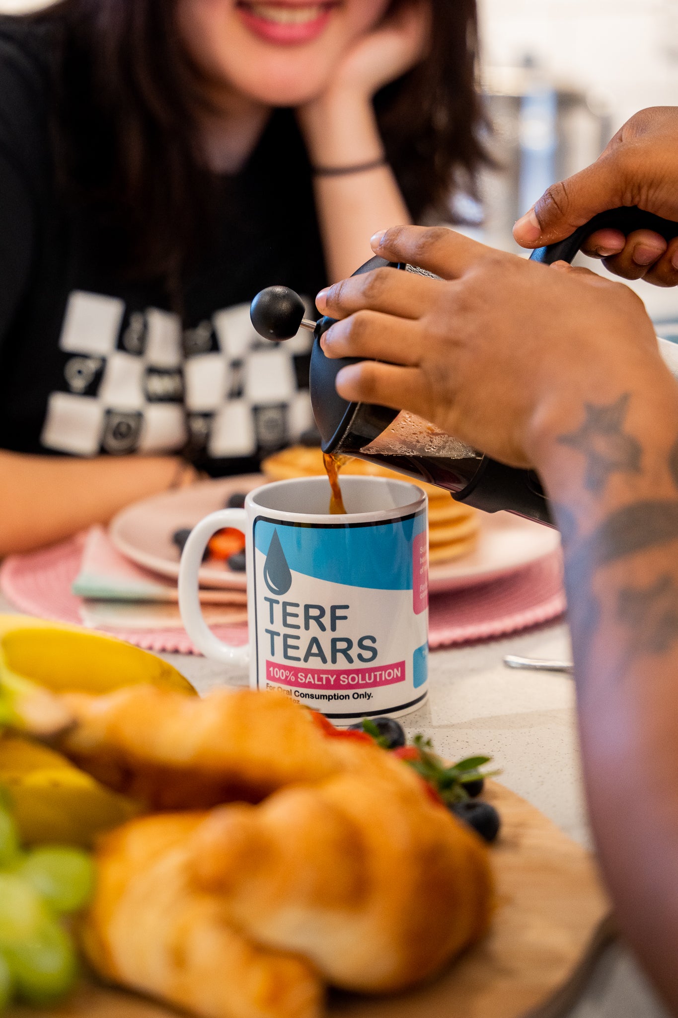 Person pouring coffee into a mug labeled 'Terf Tears' at a table with food.
