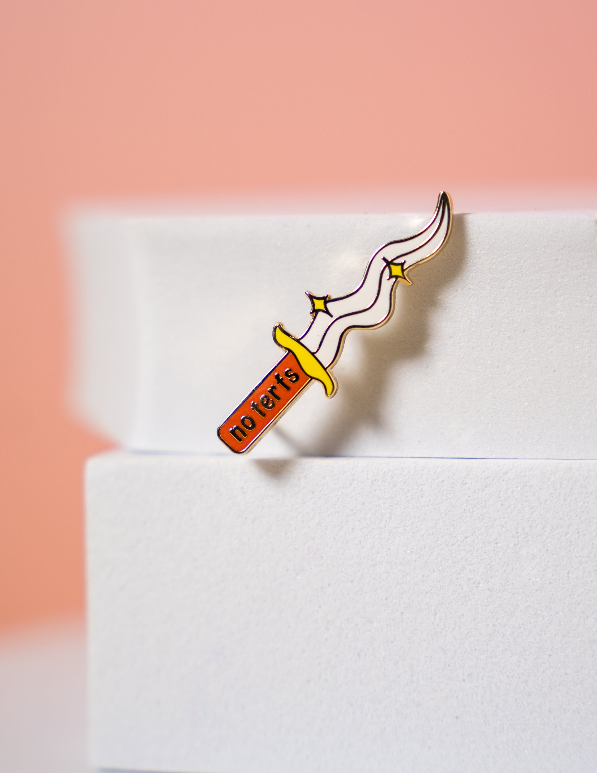A small pin in the shape of a dagger that reads "no terfs" on the handle.