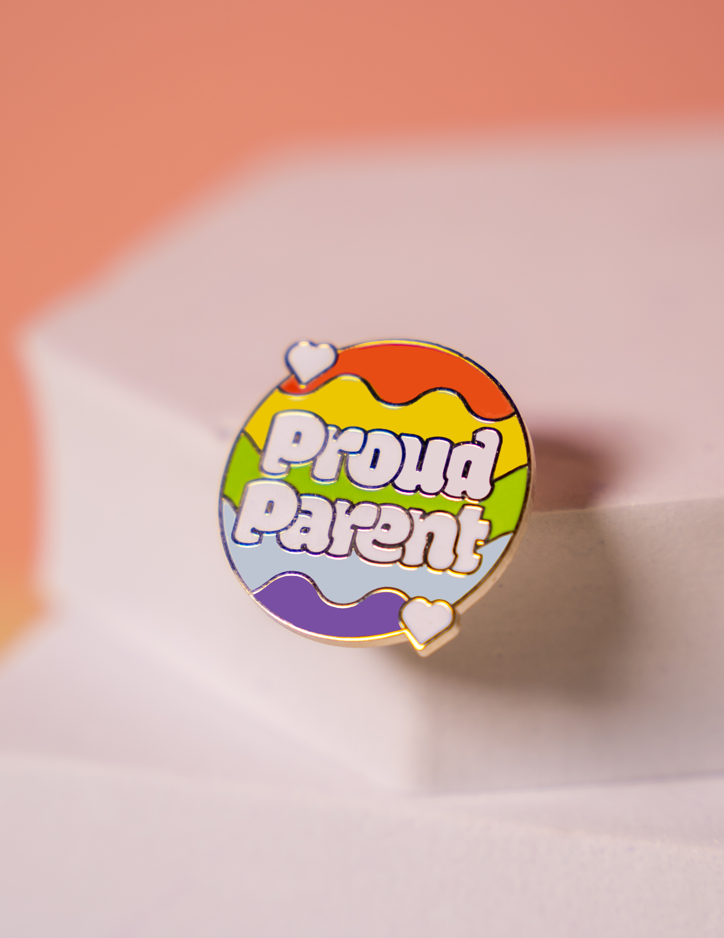 a small pin with a rainbow background reading "Proud Parent"