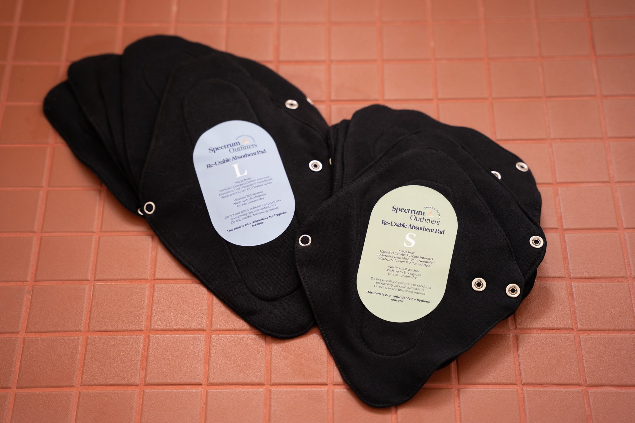 Black reusable pads with labels on a pink grid background